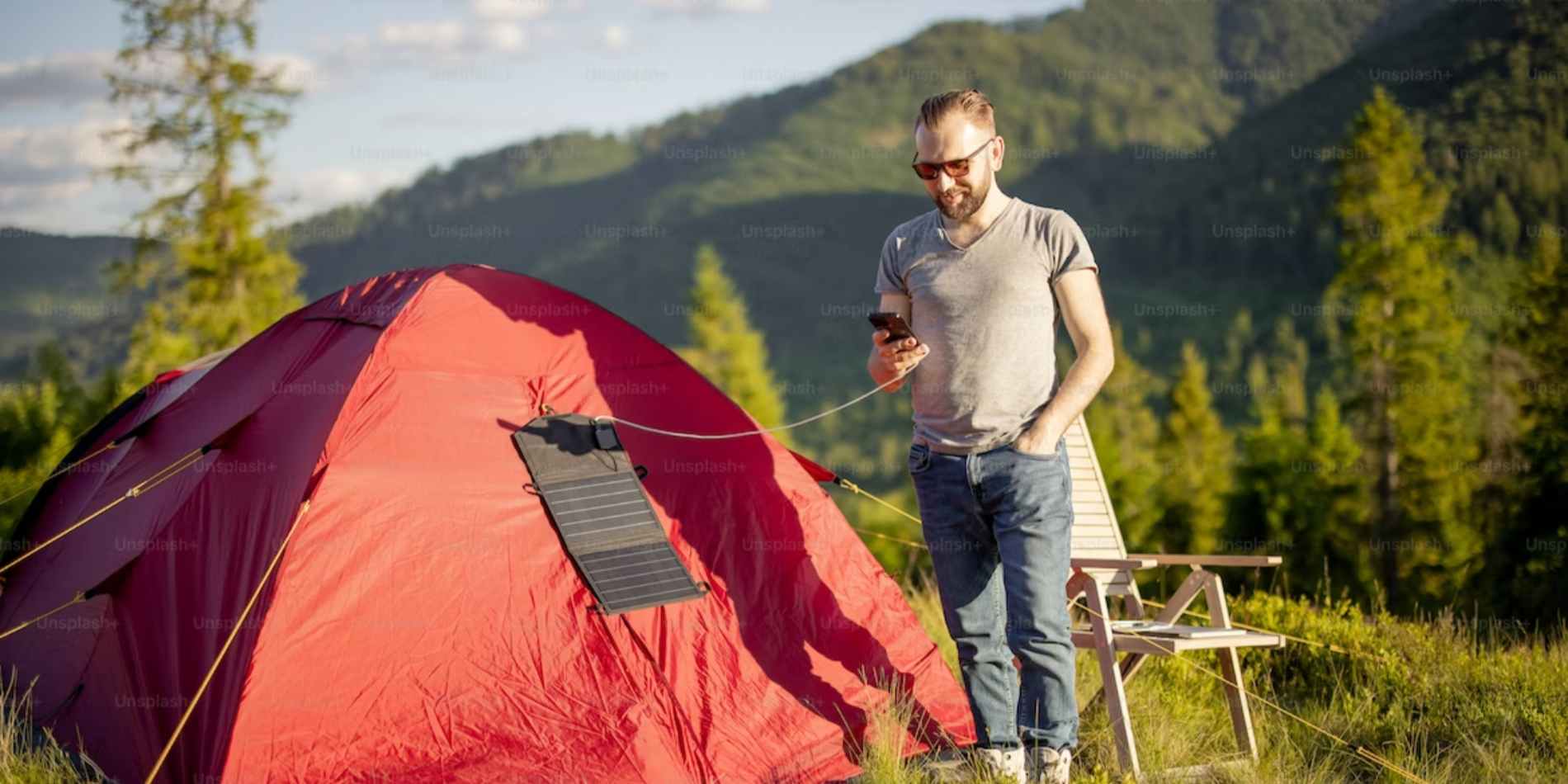 A man charging his phone from portable solar panels while camping