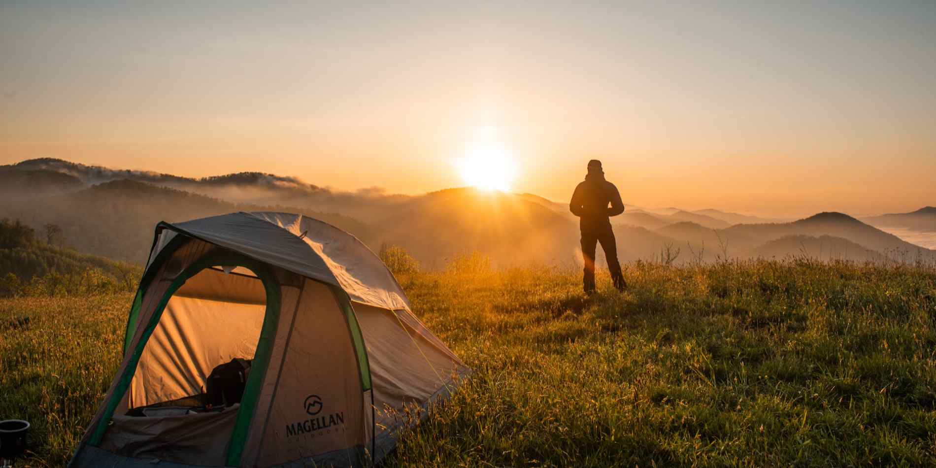 A man on the camping site facing the sun with a tent behind him